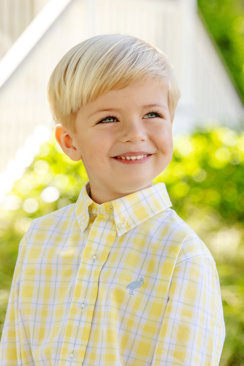 A young boy smiling while wearing a Dean’s List Dress Shirt - Forsyth Park Plaid with Beale Street Blue Stork featuring a small blue stork embroidered on the chest.