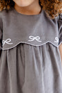 A child wearing The Beaufort Bonnet Company’s McFarland Frock in Grantley Gray Corduroy with Worth Avenue White. Only the lower part of the child’s face and upper torso are visible.