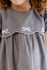 A child wearing The Beaufort Bonnet Company’s McFarland Frock in Grantley Gray Corduroy with Worth Avenue White. Only the lower part of the child’s face and upper torso are visible.