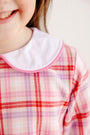A child wears The Beaufort Bonnet Company’s Lindy’s Lunch Dress in Broadway Play Plaid with Worth Avenue White, a long-sleeved plaid dress with a white rounded collar trimmed in pink.