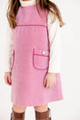 A child is wearing The Beaufort Bonnet Company’s Jill Jumper in Begley Berry Tweed over a white turtleneck shirt, paired with brown knee-high boots and a simple bracelet, standing against a white background.