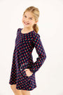 A smiling girl wears a navy blue Sadie Sweatshirt Dress - Prescott Farm Flowers with Worth Avenue White, featuring a small red flower pattern and a white-trimmed pocket.