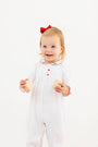 A toddler wears a Long Sleeve Britt Romper - Worth Avenue White with Holly, featuring white Pima cotton, red trim, red buttons, and a small holly embroidery on the collar, while holding two wooden blocks.