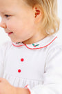 A toddler wearing a Long Sleeve Britt Romper - Worth Avenue White with Holly, a white Pima cotton romper featuring red buttons and a rounded collar embroidered with holly leaves and red berries.