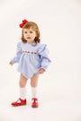 A toddler wears The Beaufort Bonnet Company Long Sleeve Ruehling Ruffle Bubble - Park City Periwinkle Ticking Stripe & Worth Avenue White, a blue and white striped long sleeve romper with floral embroidery, white socks, and red shoes.