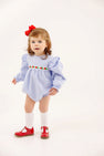 A toddler wears The Beaufort Bonnet Company Long Sleeve Ruehling Ruffle Bubble - Park City Periwinkle Ticking Stripe & Worth Avenue White, a blue and white striped long sleeve romper with floral embroidery, white socks, and red shoes.