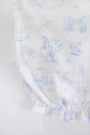 Experience the charm of The Beaufort Bonnet Company’s Sir Proper’s Sweet Arrival (Beale Street Blue) Bundle, featuring white fabric adorned with light blue illustrations of animals riding bikes, flying with balloons, and playing near trees and water. This adorable everyday set includes a layette gown with a ruffled edge at the bottom—making it a delightful baby shower gift. The bundle also comes complete with the lovable Bradley Bear for an extra special touch.
