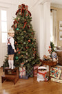 A young boy in Peabody Prep Short - Nantucket Navy Corduroy with Society Prep Plaid shorts stands on a step stool to decorate a Christmas tree.