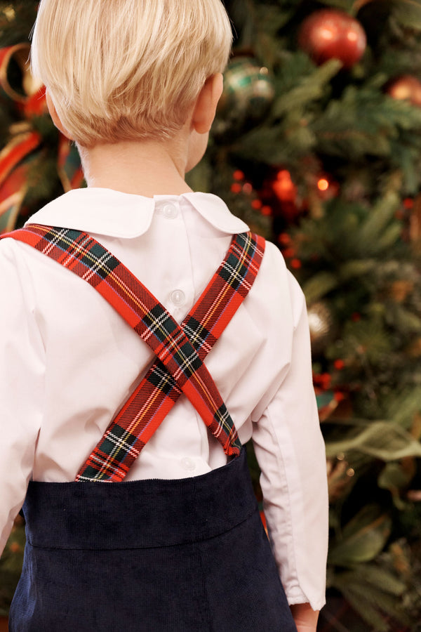 A young child wears a white collared shirt with red plaid crisscross suspenders over Peabody Prep Short - Nantucket Navy Corduroy with Society Prep Plaid, standing in front of a Christmas tree.