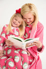 A woman and a young girl read a book together while wearing matching Payton Pajama Set - Distinguished Doggies with Hamptons Hot Pink cotton pajamas featuring dog prints.