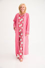A smiling woman wears a cozy, long Rest Awhile Robe - Richmond Red & Hamptons Hot Pink over matching pajamas patterned with illustrated Santa Claus faces.