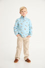 A young boy with blond hair stands with his hands in his pockets, wearing The Beaufort Bonnet Company’s Pendleton’s Popped Collar - Fine Weather For Ducks with Grantley Gray polo shirt, paired with beige pants and brown shoes, against a plain white background.