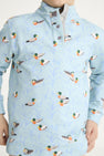 A child models The Beaufort Bonnet Company’s “Pendleton’s Popped Collar - Fine Weather For Ducks with Grantley Gray,” a light blue boys polo shirt adorned with mallard duck illustrations in flight and on the water. The shirt features a buttoned collar; the child’s face is partially out of frame.
