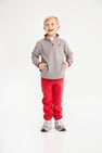 A smiling young boy wears a Hayword Half-Zip (Fleece) - Grantley Gray with Richmond Red, paired with red sweatpants and gray sneakers.