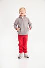 A smiling young boy wears a Hayword Half-Zip (Fleece) - Grantley Gray with Richmond Red, paired with red sweatpants and gray sneakers.
