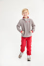 A young boy in a cozy Hayword Half-Zip (Fleece) - Grantley Gray with Richmond Red and matching sweatpants stands with his hands in his pockets.