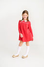 A smiling girl wears a red long-sleeved The Beaufort Bonnet Company dress with a white collar and Jefferies High Class Knee Socks - White.