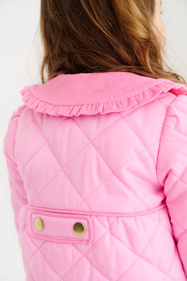 A child wearing a Maude’s Carlyle Quilted Coat in Hamptons Hot Pink with Palm Beach Pink, featuring a ruffled collar and a back tab with two gold buttons.
