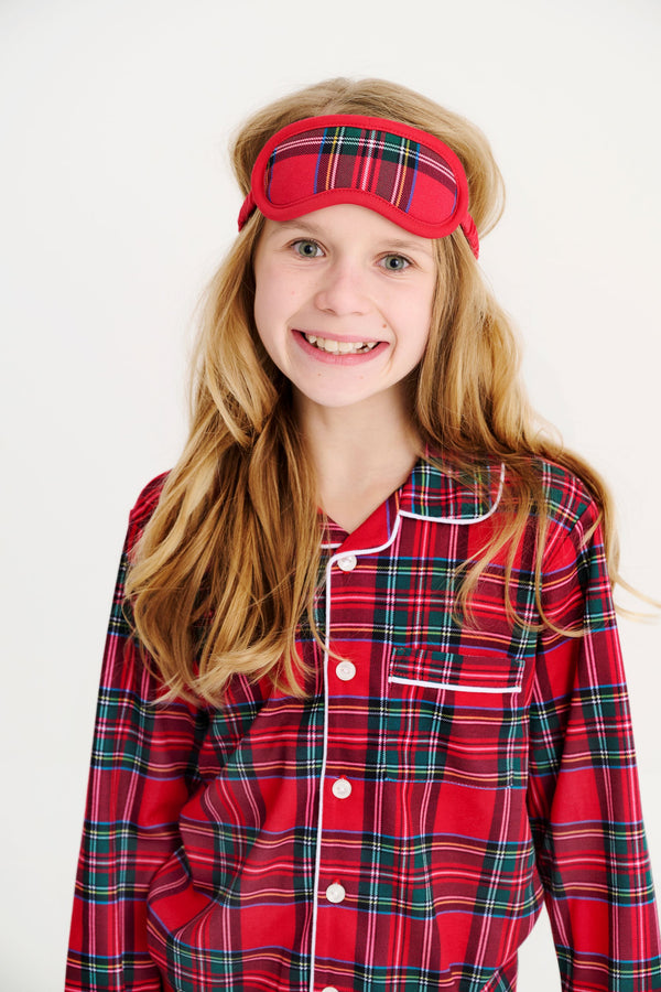 A smiling girl wears a Lock’s Little Set - Society Prep Plaid with Worth Avenue White red plaid pajama set with a matching sleep mask for the holidays.