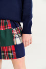 A person wearing an Isabelle’s Sweater - Nantucket Navy with Brass Buttons paired with a skirt featuring a multi-colored plaid patchwork pattern.