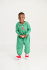 A young child smiles while standing in The Beaufort Bonnet Company’s Long Sleeve Bradford Romper - Kiawah Kelly Green with Stocking Embroidery, paired with red sneakers, against a plain white background.