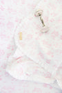 A silver rattle rests on The Beaufort Bonnet Company’s Sir Proper’s Sweet Arrival (Hamptons Hot Pink) Baby Buggy Blanket, made from pima cotton with pink animal and nature prints, ruffled edges, and a yellow label stitched in the corner.