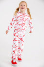 A young girl wears a white, quilted Georganna Jacket - Quilted Bonnie Scot Bows and matching joggers patterned with pink and red bows, paired with red sneakers.