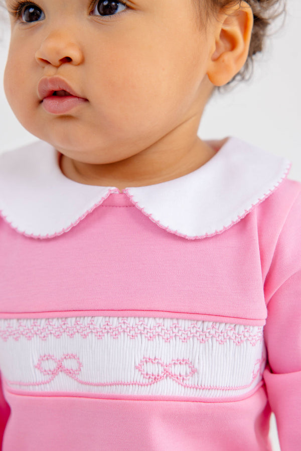 Close-up of a baby wearing a Rigsby Romper - Hamptons Hot Pink with Worth Avenue White and Bow Smocking, featuring a white Peter Pan collar and white bow smocking across the chest.
