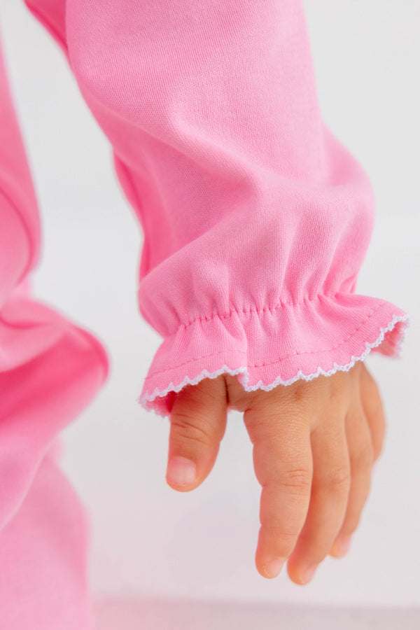 Close-up of a toddler’s hand resting on the ruffled, white picot-trimmed sleeve of a Rigsby Romper - Hamptons Hot Pink with Worth Avenue White and Bow Smocking.