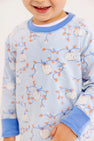 A smiling child wears The Beaufort Bonnet Company Cassidy Comfy Crewneck – Gourd-geous (Buckhead Blue) with Sunrise Blvd Blue, featuring a white, orange, and blue pumpkin and vine design. Only the lower half of the face and upper body are visible.