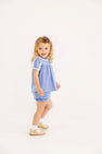 A young girl wears a Mary Baker Bloomer Set - Park City Periwinkle with Worth Avenue White in Pima Cotton Knit with white lace trim, a white hair bow, white socks, and tan shoes.