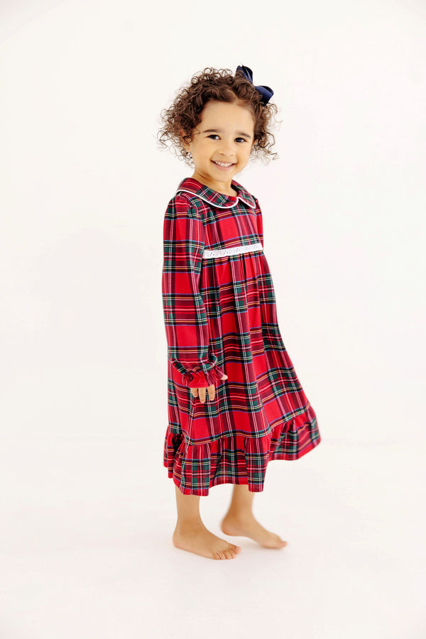 A young girl smiling while wearing a Goldie Locks Nightgown - Society Prep Plaid with Worth Avenue White in red, green, and white with a white collar and trim.