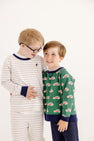 Two young boys stand together, smiling. One wears glasses and striped pajamas, while the other is dressed in The Beaufort Bonnet Company’s Cassidy & Gates Sweat Set in Keeneland Khaki Stripe & Nantucket Navy. They appear happy on a plain white background.