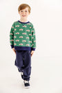 A young child with brown hair smiles, wearing The Beaufort Bonnet Company’s Smitty Sweatshirt in Windsor Wagon (Grier Green) featuring red car prints and a cozy fleece interior, paired with Nantucket Navy pants and dark sneakers, standing against a plain white background.