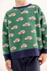 A child wears The Beaufort Bonnet Company’s Smitty Sweatshirt in Windsor Wagon (Grier Green) with Nantucket Navy, featuring a repeating red and white car print, navy cuffs, and a cozy fleece interior, paired with navy pants. The child’s face is not visible.