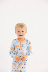 A young child with blonde hair is wearing The Beaufort Bonnet Company’s Payton Pajama Set – Candy & Critters (Buckhead Blue) with Seashore Sherbet, smiling against a plain white background.