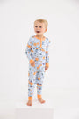 A smiling young child stands barefoot on a white block against a plain white background, modeling the cozy Payton Pajama Set - Candy & Critters (Buckhead Blue) with Seashore Sherbet by The Beaufort Bonnet Company, featuring colorful Halloween-themed prints—perfect sleepwear for boys.