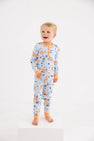 A smiling young child stands barefoot on a white block against a plain white background, modeling the cozy Payton Pajama Set - Candy & Critters (Buckhead Blue) with Seashore Sherbet by The Beaufort Bonnet Company, featuring colorful Halloween-themed prints—perfect sleepwear for boys.