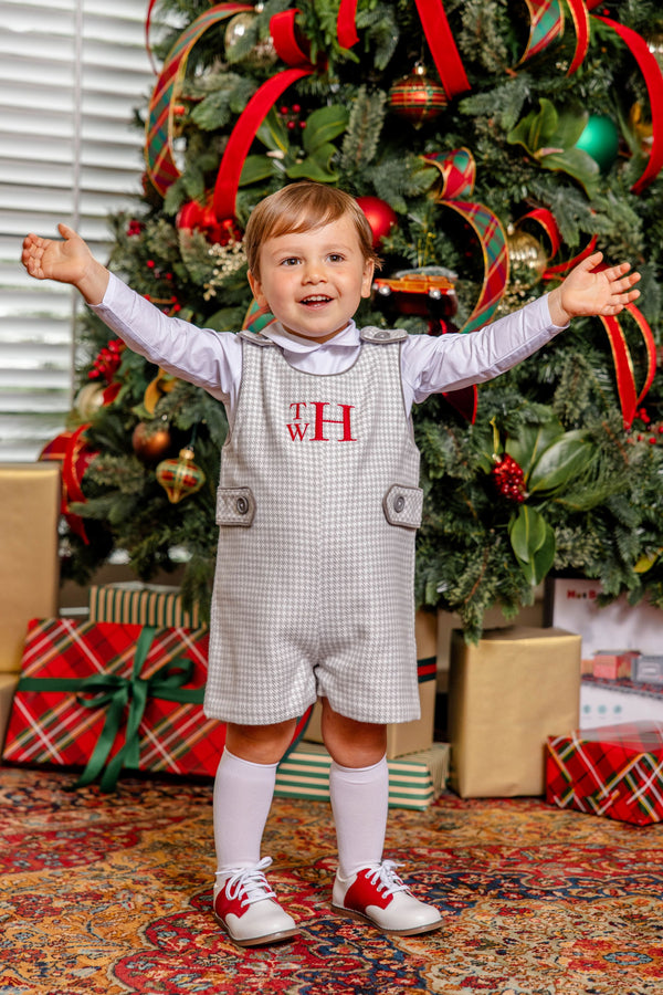 A young boy stands with his arms outstretched in front of a Christmas tree for a winter portrait, wearing a white long-sleeved shirt and a Jack Keene Jon Jon - Grantley Gray Houndstooth with Grantley Gray.