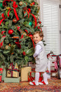 A young boy wearing a Jack Keene Jon Jon - Grantley Gray Houndstooth with Grantley Gray, a white shirt, and red and white shoes stands smiling in front of a decorated Christmas tree for a winter family portrait.
