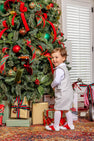 A young boy wearing a Jack Keene Jon Jon - Grantley Gray Houndstooth with Grantley Gray, a white shirt, and red and white shoes stands smiling in front of a decorated Christmas tree for a winter family portrait.