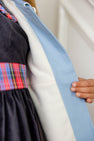 A person wearing a dark dress with a plaid belt holds open The Beaufort Bonnet Company’s Pippa Peacoat in Barrington Blue with Palmetto Pearl, revealing its light blue and white inner lining.