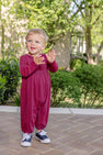 A toddler wearing a Long Sleeve Bradford Romper - Richmond Red and Nantucket Navy Stripe and sneakers claps their hands while standing on a brick patio.