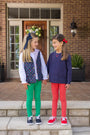 Two young girls hold hands on a porch, one wearing a Vaughn Vest - Prescott Farm Flowers with Richmond Red Microdot and green leggings, the other in a navy sweatshirt and red leggings.