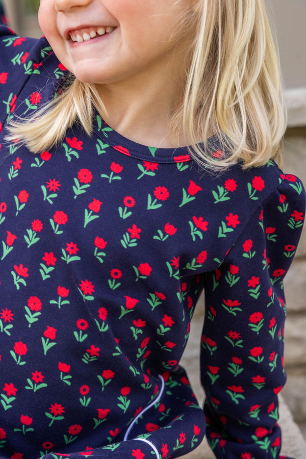 A young child wearing a navy blue Sadie Sweatshirt Dress - Prescott Farm Flowers with Worth Avenue White, patterned with small red flowers and green stems.