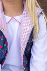 A child wears Emma’s Elbow Patch Top - Worth Avenue White with Richmond Red Flowers, a long-sleeved Pima cotton shirt under a navy blue quilted vest featuring red flower patterns, a red-and-white polka dot lining, and elbow patches.