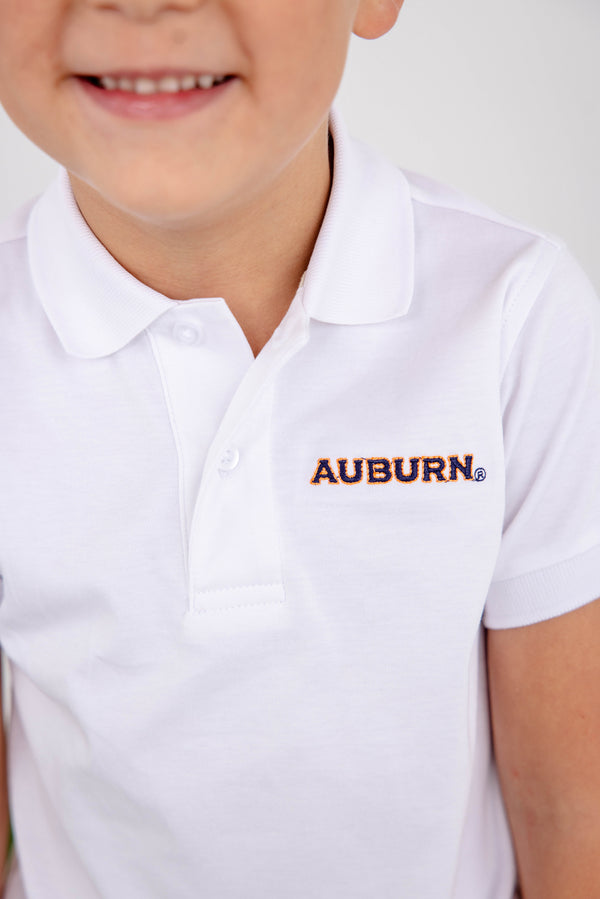 A smiling child wears The Beaufort Bonnet Company’s Auburn Prim & Proper Polo in Worth Avenue White, crafted from soft Pima cotton and featuring the embroidered Auburn logo in orange and blue letters.