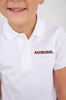 A smiling child wears The Beaufort Bonnet Company’s Auburn Prim & Proper Polo in Worth Avenue White, crafted from soft Pima cotton and featuring the embroidered Auburn logo in orange and blue letters.