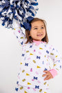 A young child with a blue bow smiles while holding blue and white pom-poms aloft. Dressed in The Beaufort Bonnet Company’s Michigan Cassidy Comfy Crewneck—Bold in Blue with Hamptons Hot Pink—this outfit showcases University of Michigan pride with fun symbols and is the perfect choice for gameday excitement.