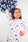A young child with a blue bow smiles while holding blue and white pom-poms aloft. Dressed in The Beaufort Bonnet Company’s Michigan Cassidy Comfy Crewneck—Bold in Blue with Hamptons Hot Pink—this outfit showcases University of Michigan pride with fun symbols and is the perfect choice for gameday excitement.